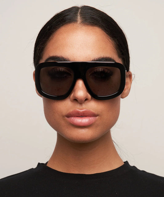 Person wearing black sunglasses and a black top against a plain background