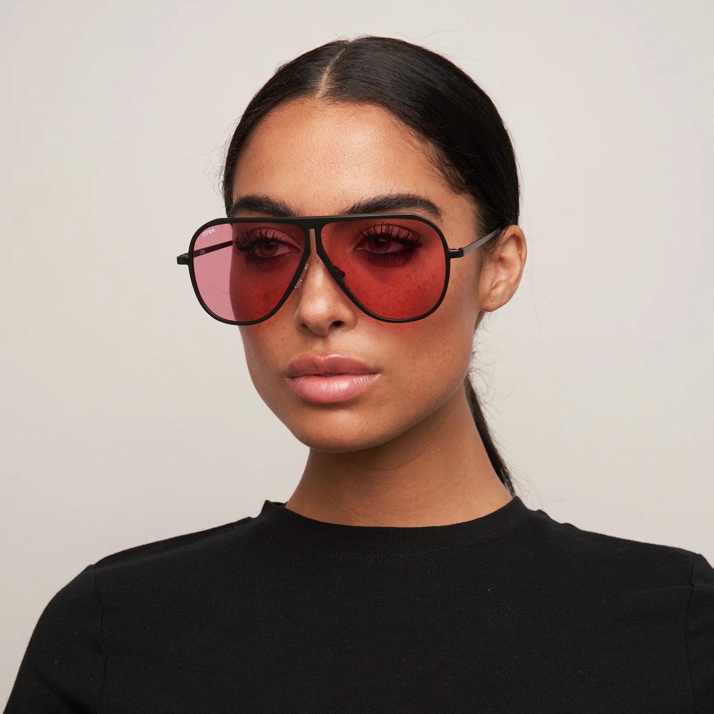 Woman wearing a black t-shirt and red sunglasses against a plain background