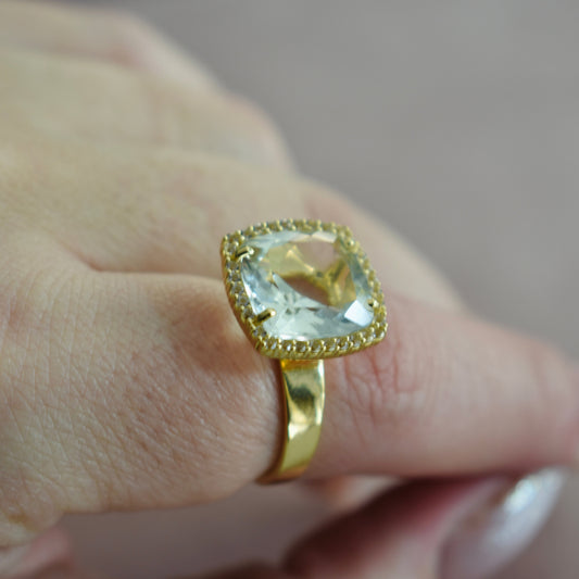 Gold ring with a large gemstone on a finger against a neutral background