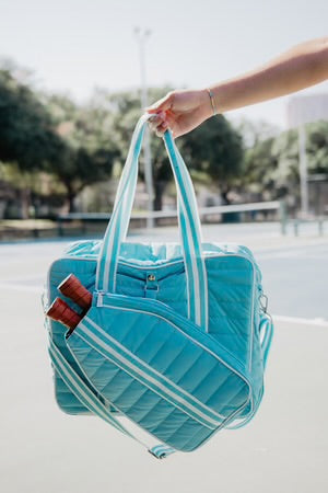 Turquoise duffel bag with white straps held by a person outdoors.