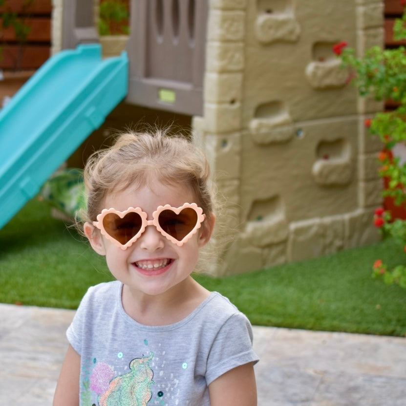 Young girl wearing heart-shaped sunglasses in front of a playground.