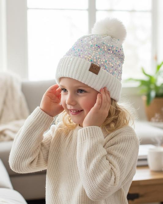 Child wearing a white knit sweater and a decorative beanie with sequins indoors.