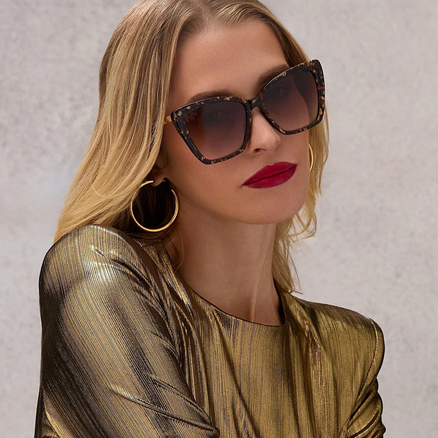 Woman wearing sunglasses and a gold outfit against a neutral background