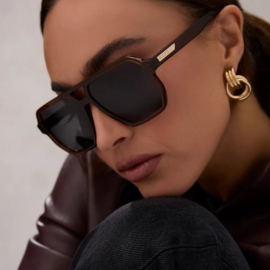 Close-up of a person wearing sunglasses and gold earrings against a neutral background