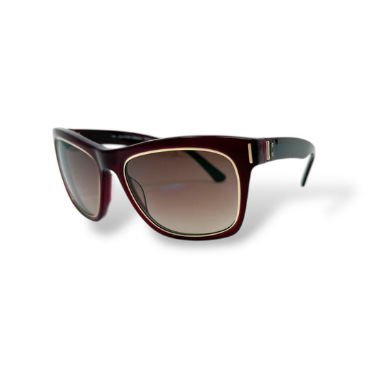 A pair of Calvin Klein sunglasses with burgundy frames and gold details, featuring black gradient lenses.
