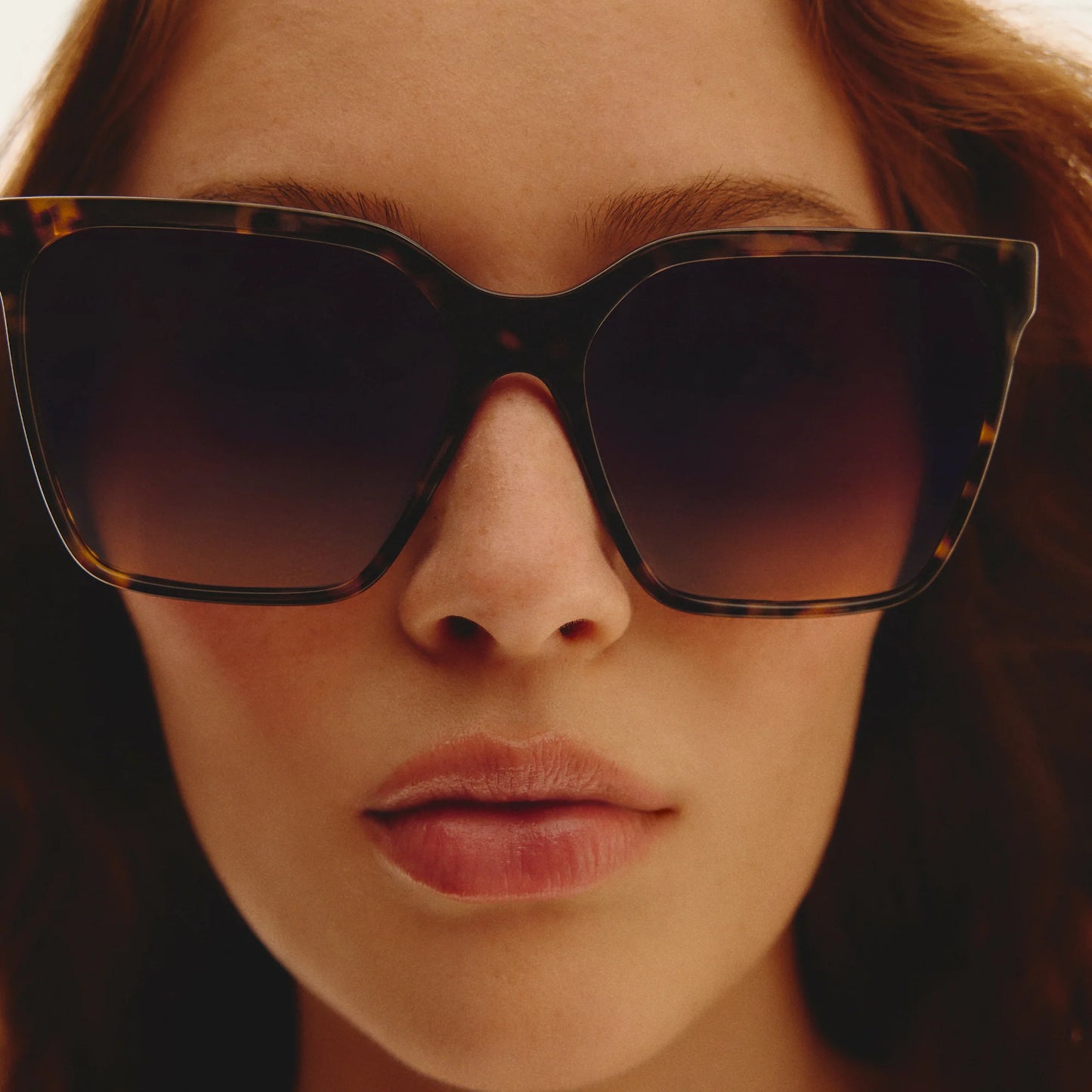 Close-up of a person wearing tortoiseshell sunglasses with a blurred background