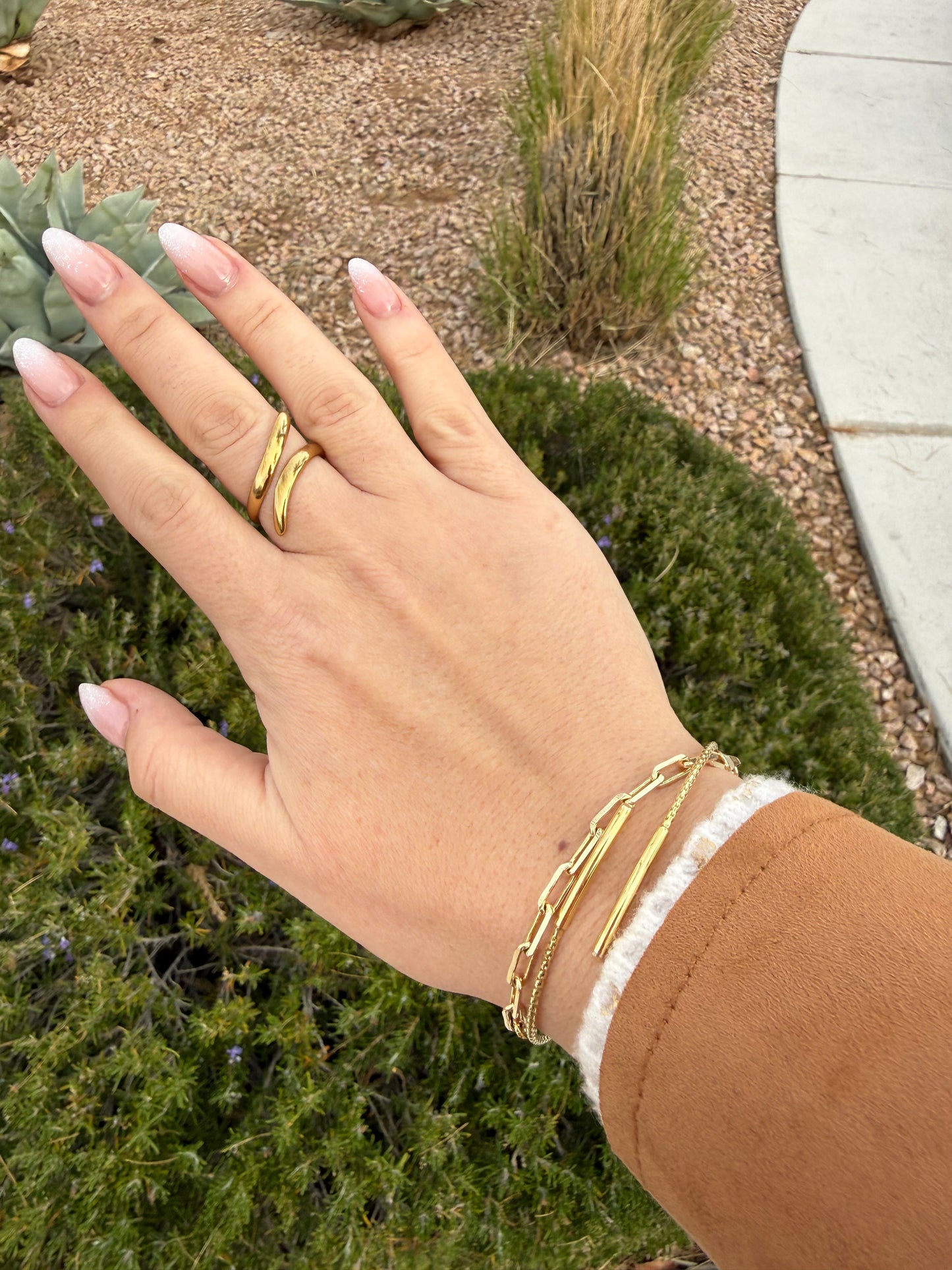 Hand wearing gold rings and bracelets with a blurred outdoor background