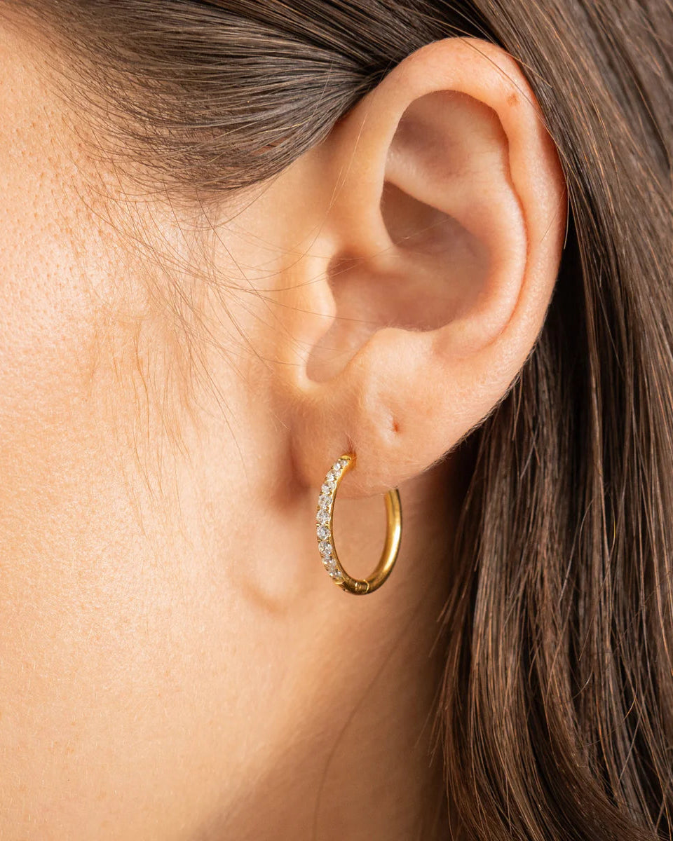 Close-up of an ear wearing a gold hoop earring with clear stones.