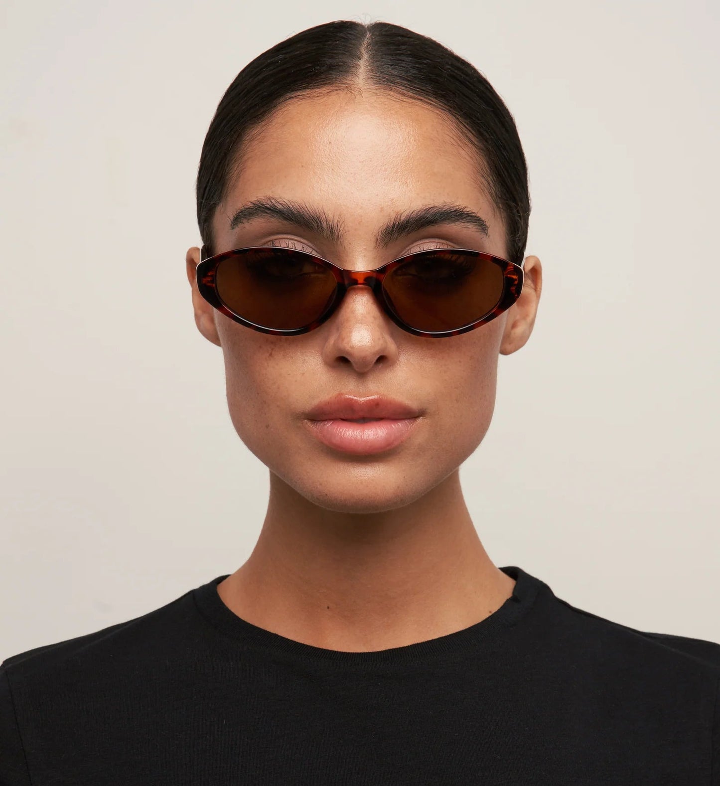 Person wearing brown sunglasses and a black shirt against a plain background