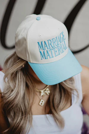 Person wearing a cap with 'Marriage Material' text in turquoise on a beige background