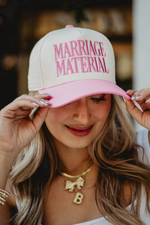 Woman wearing a cap with 'MARRIAGE MATERIAL' text, blurred background