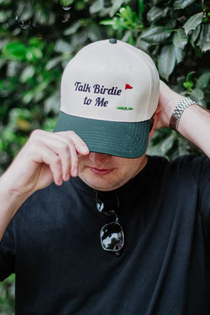 Person wearing a cap with 'Talk Birdie to Me' text against a green leafy background
