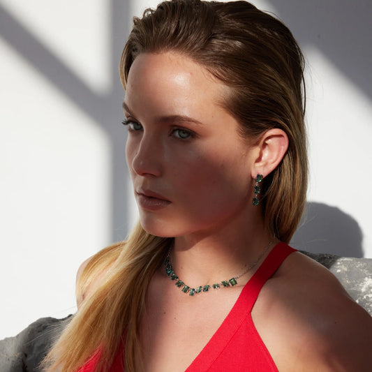 Woman wearing a red dress and green jewelry against a neutral background