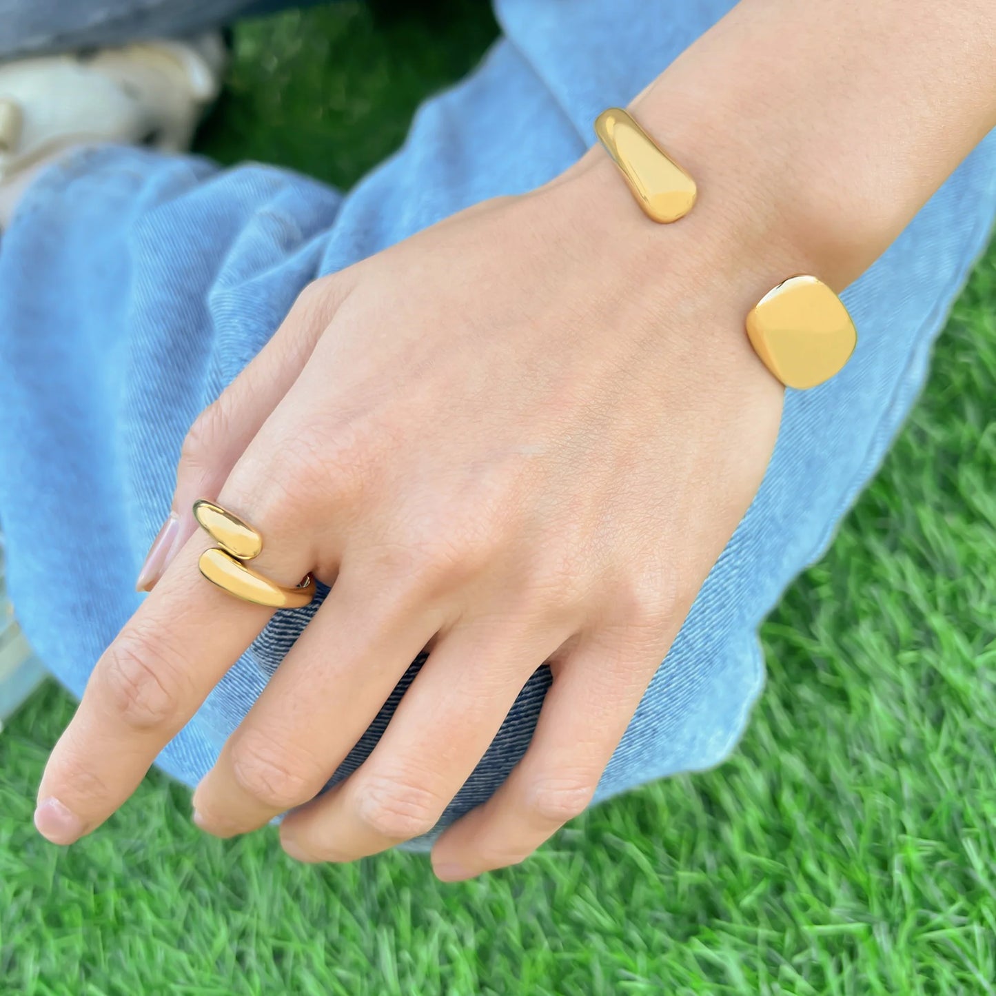 Gold bracelet and ring on a hand with grass background