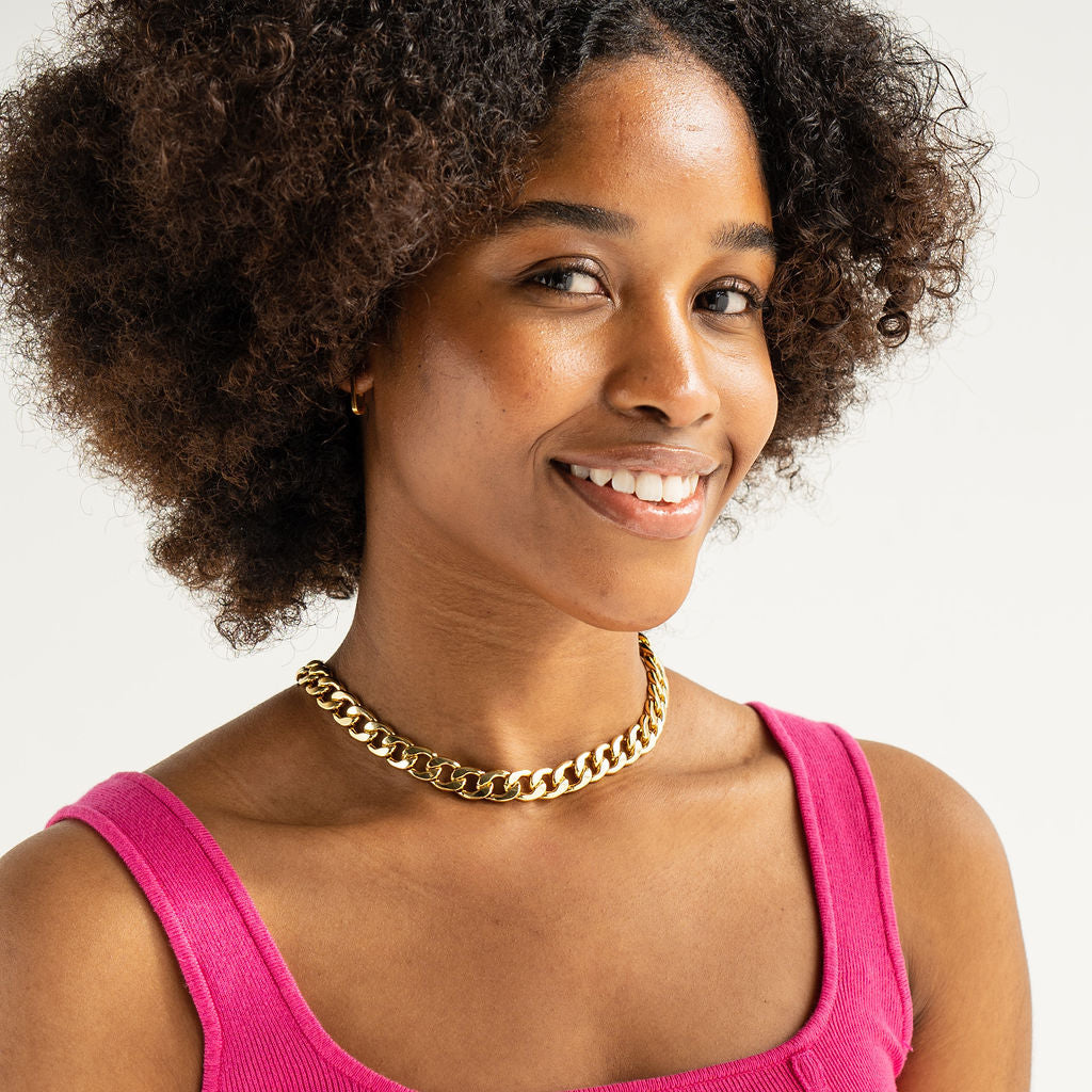Woman wearing a pink top and gold necklace against a plain background