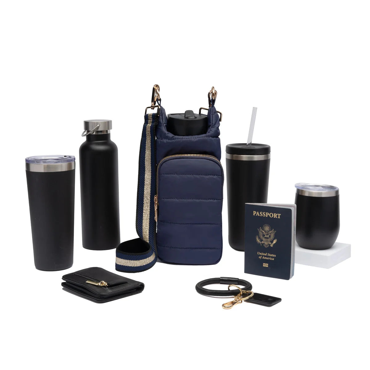 Collection of travel accessories including a navy crossbody bag, black tumblers, and a passport on a white background.