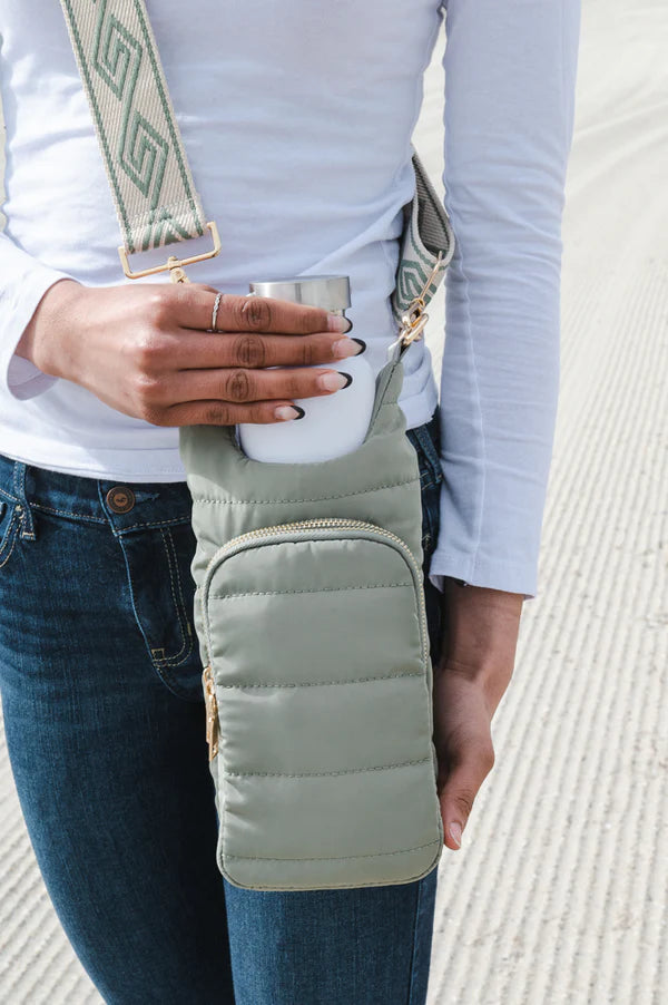 Person holding a cup with a green puffer bag over their shoulder on a light background