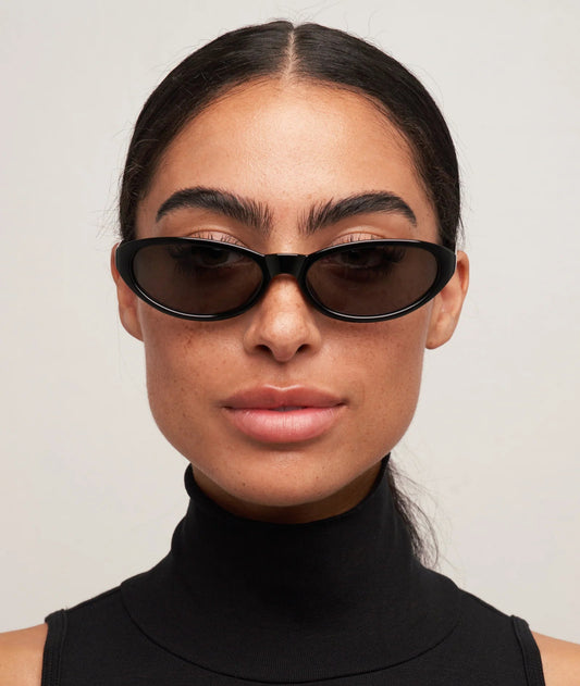 Woman wearing black sunglasses and a black turtleneck against a light gray background