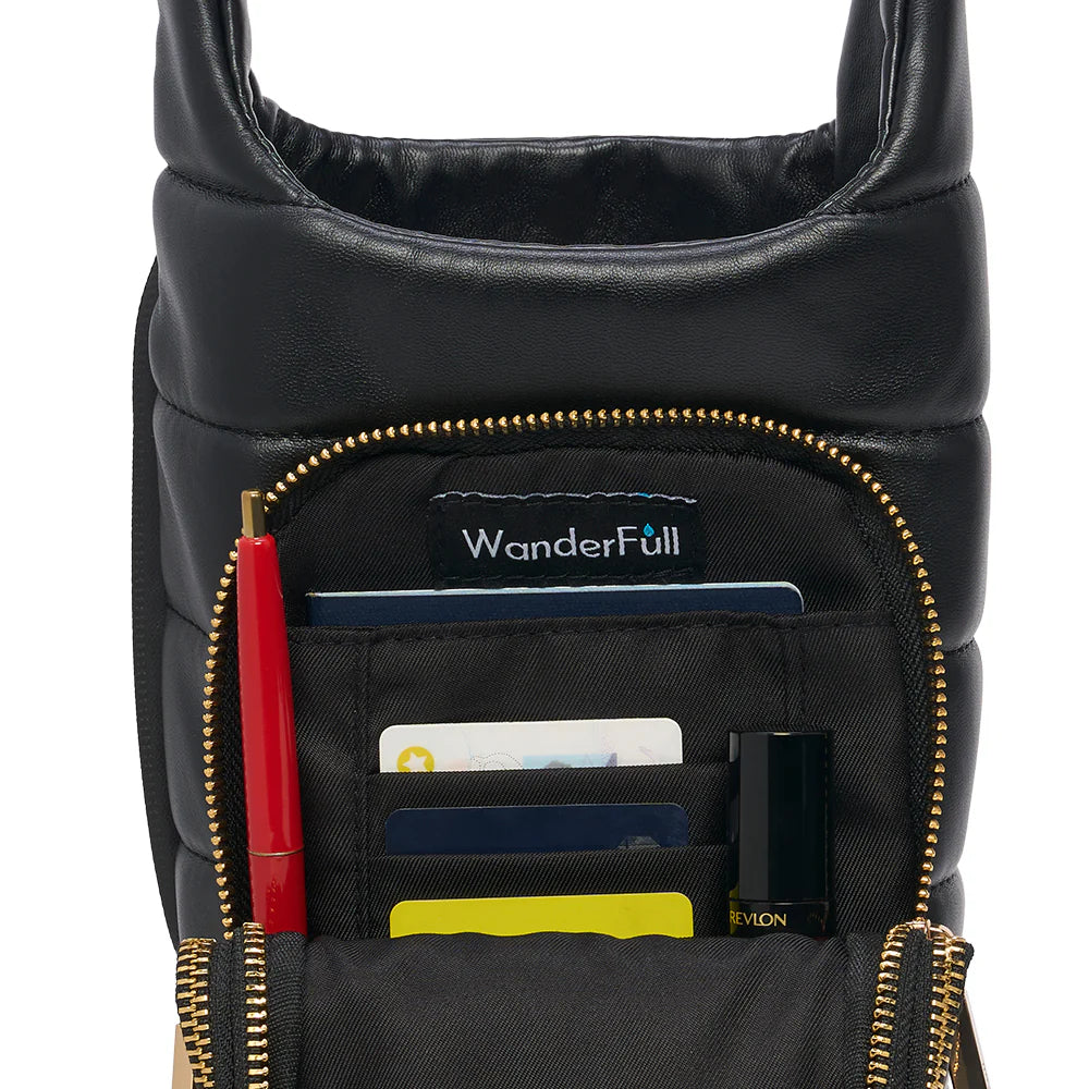 Black bag with gold zippers showing various items including a red pen, cards, and a bottle.