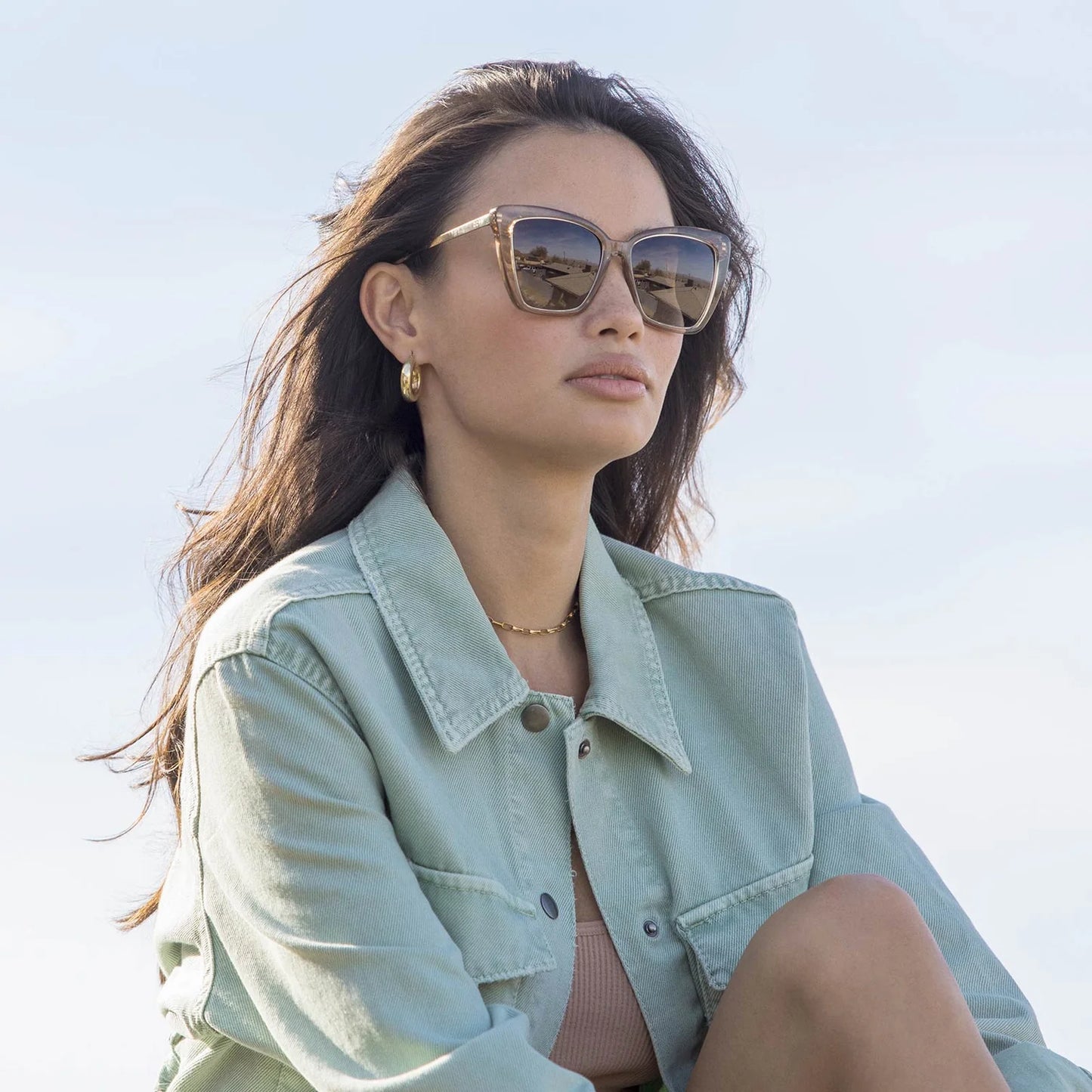 Woman wearing sunglasses and a light green jacket against a clear blue sky