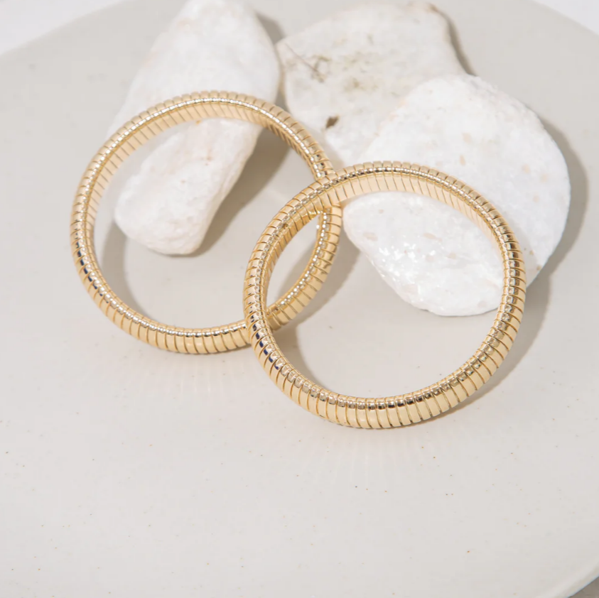 Gold snake bangles on a white surface with seashells