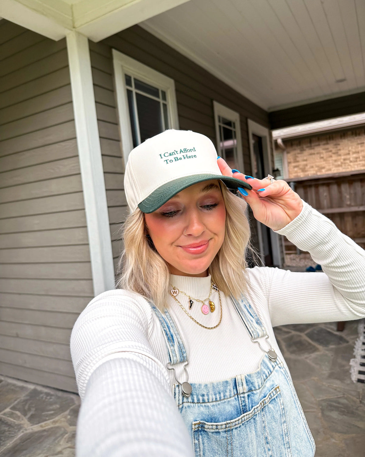 Woman wearing a cap and overalls standing on a porch