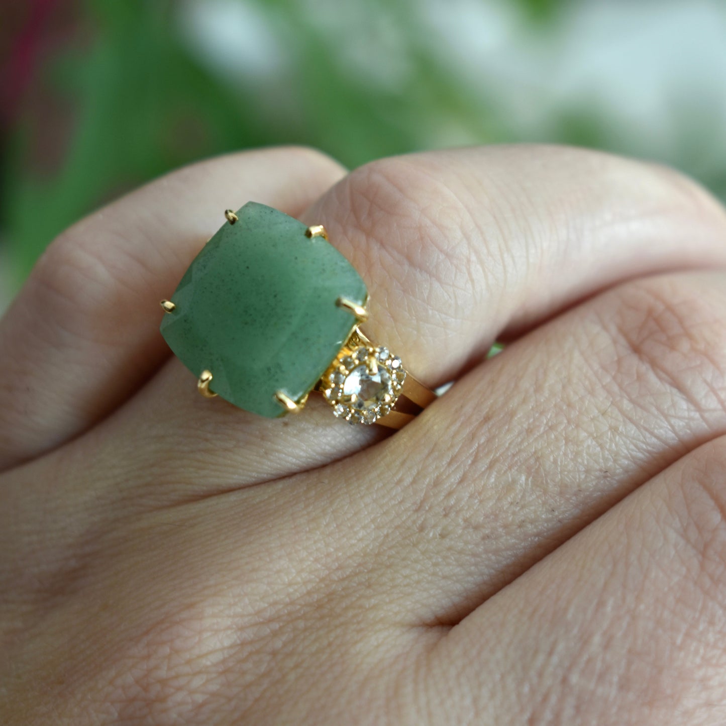Green ring with gold accents on a finger against a blurred natural background