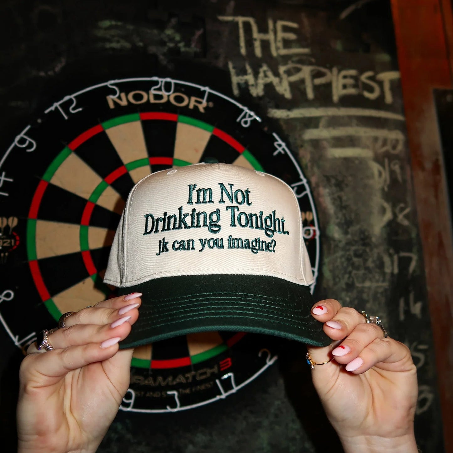 Person holding a cap with text in front of a dartboard with 'The Happiest Number' written on it.