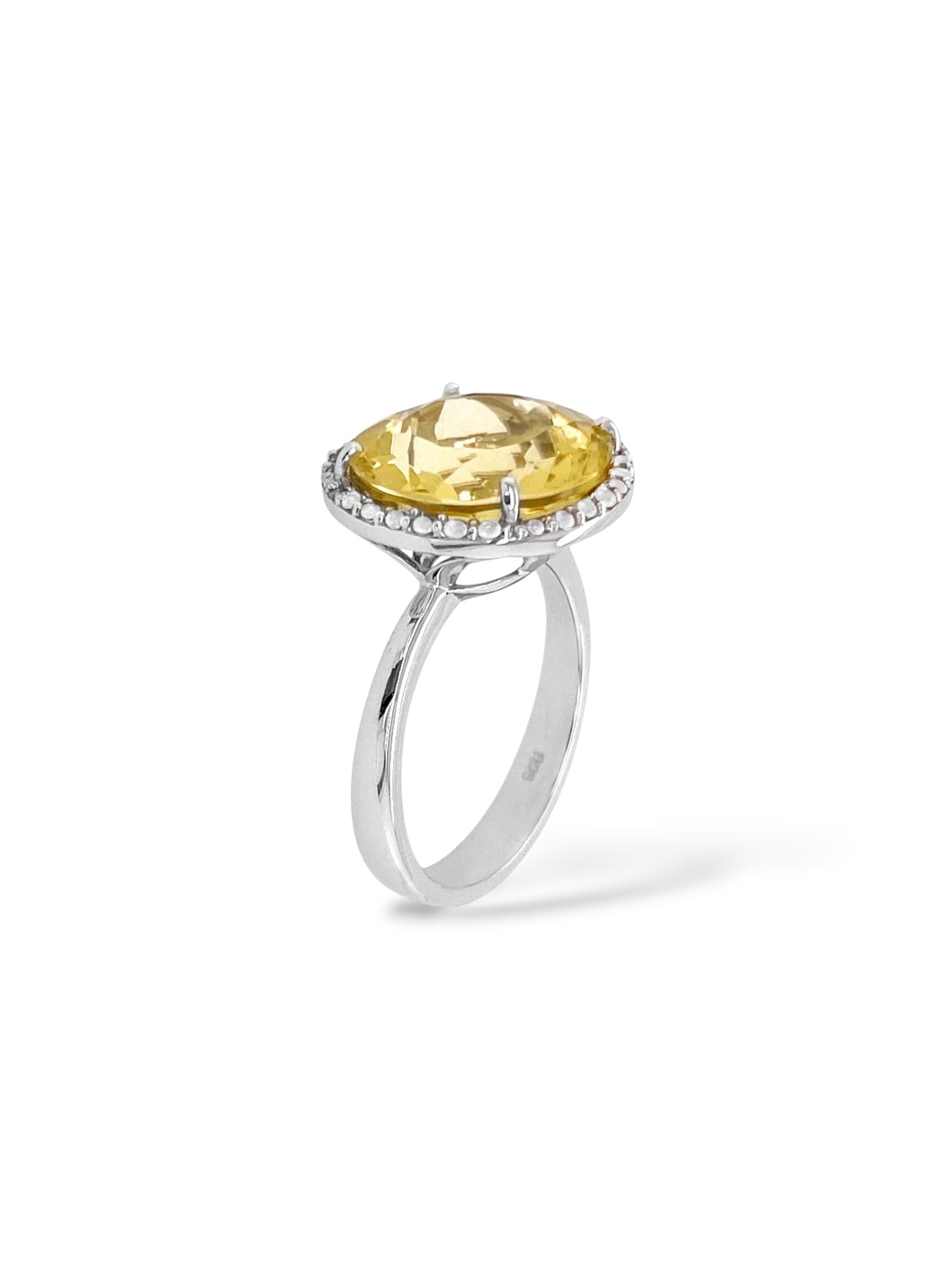 A silver ring featuring a large round-cut yellow gemstone in a prong setting, surrounded by a halo of small clear stones, shown on a white background.