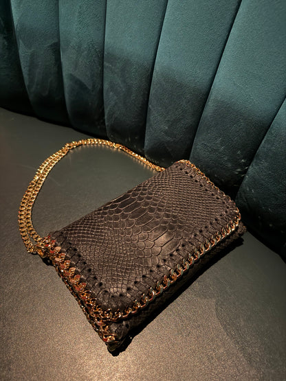 Black croc textured clutch bag with gold chain on a dark background