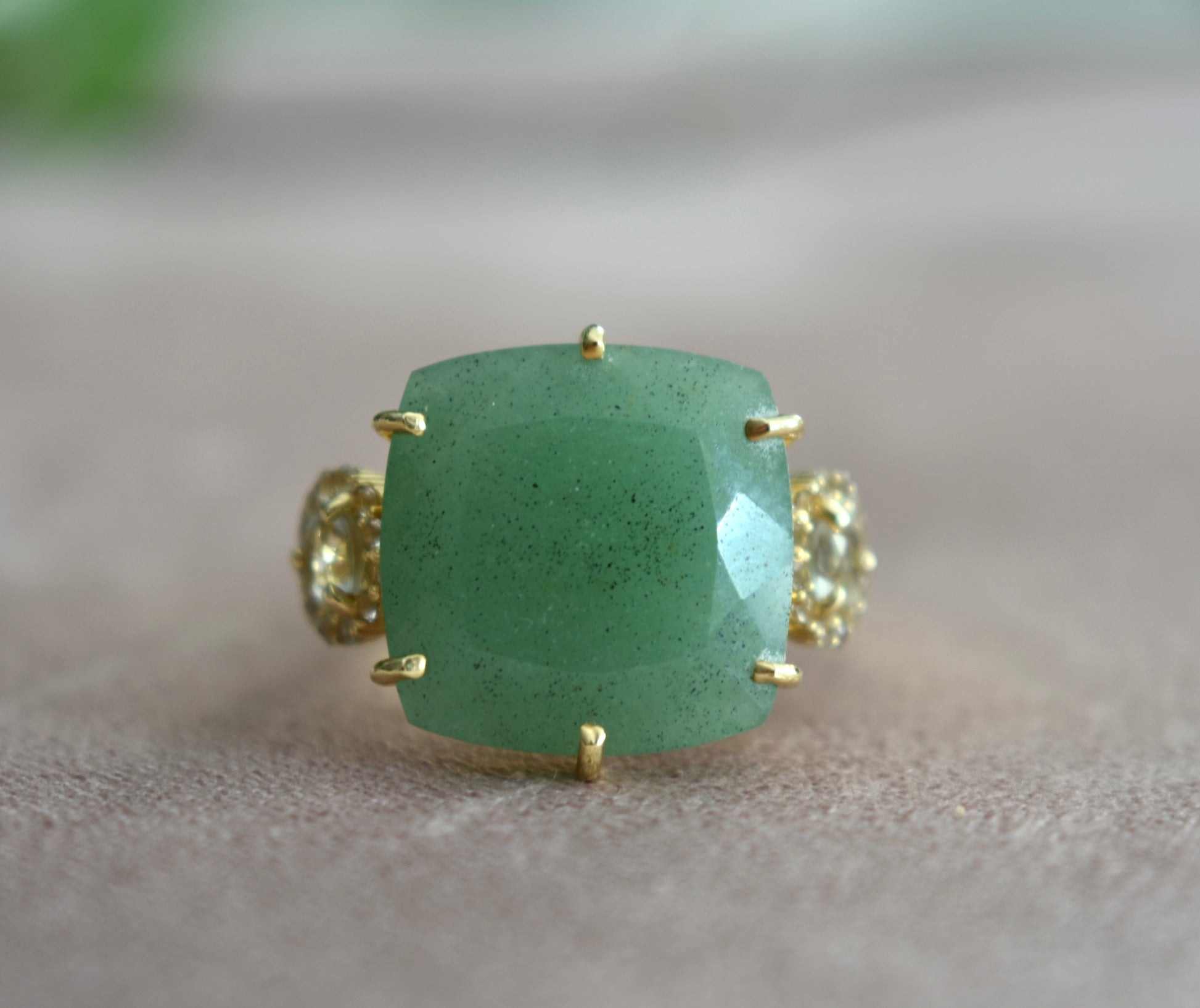 Green gemstone ring with gold accents on a neutral background