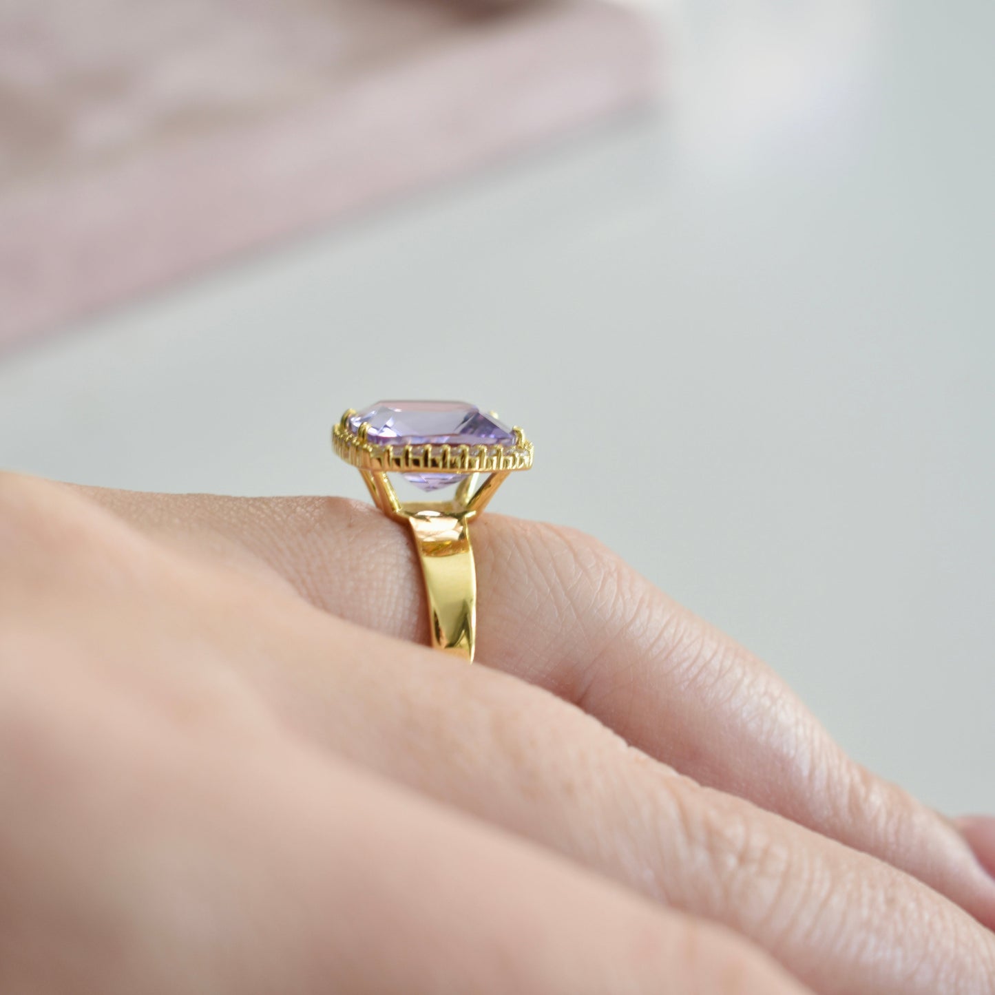 Gold ring with a purple gemstone on a hand against a neutral background