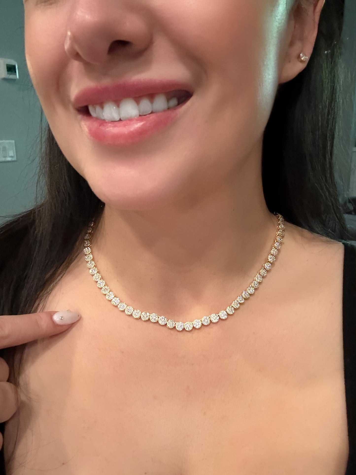 Close-up of a person wearing a diamond necklace, with a neutral background.