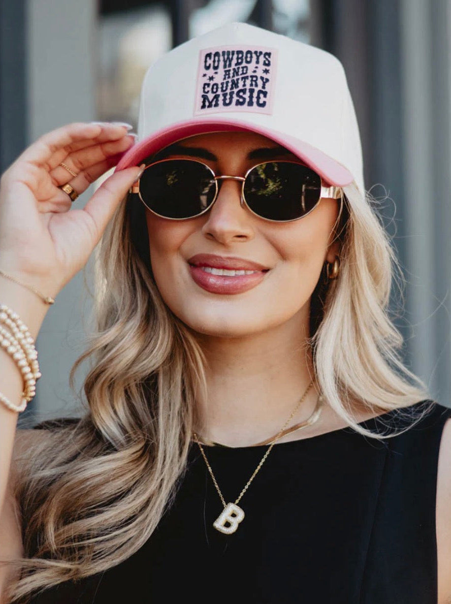 Woman wearing a pink cap with text and sunglasses, outdoors.