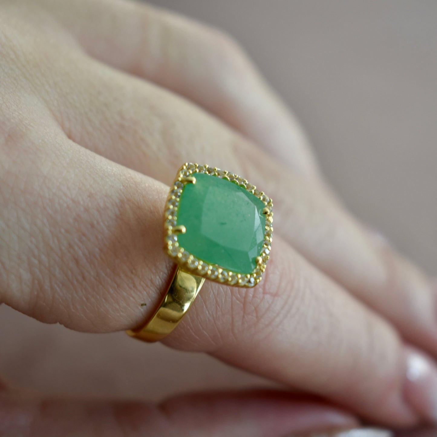 Gold ring with a green gemstone on a finger against a neutral background