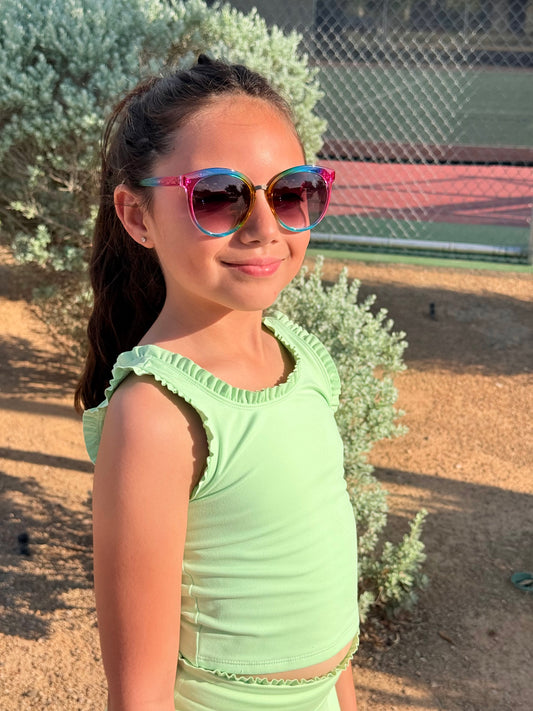 Young girl wearing colorful sunglasses and a light green top outdoors.