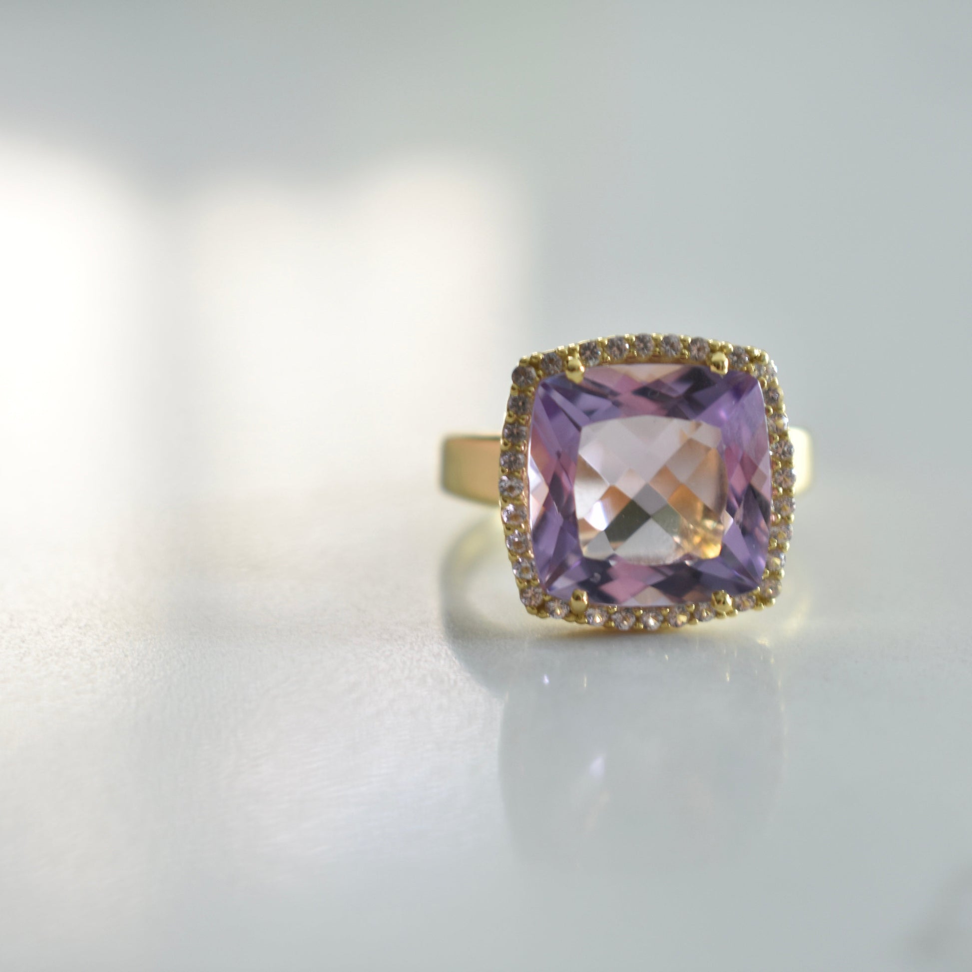 Gold ring with a large purple gemstone on a light gray background