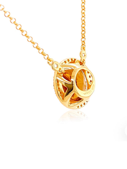 A gold pendant necklace featuring a circular, openwork design with a warm amber-orange center, suspended from a delicate gold chain on a white background.