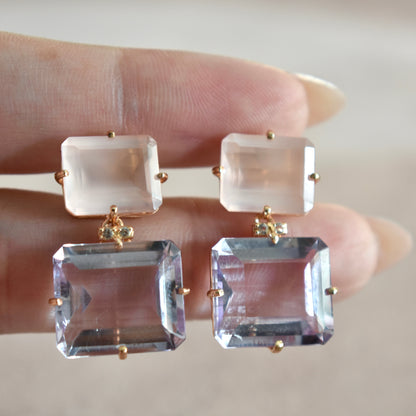 Pair of earrings with clear gemstones held between fingers against a neutral background
