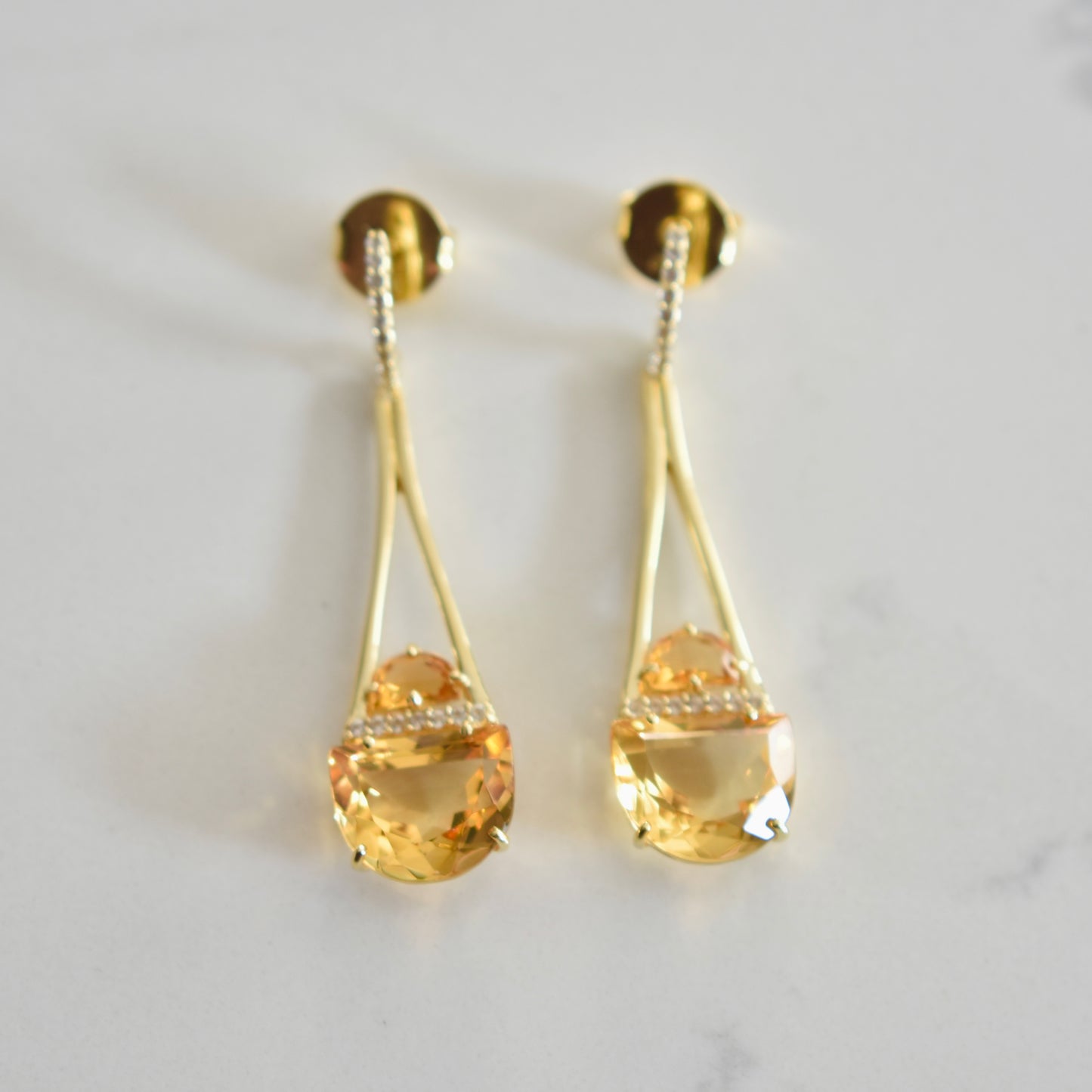 Gold earrings with teardrop-shaped citrine stones on a light gray background