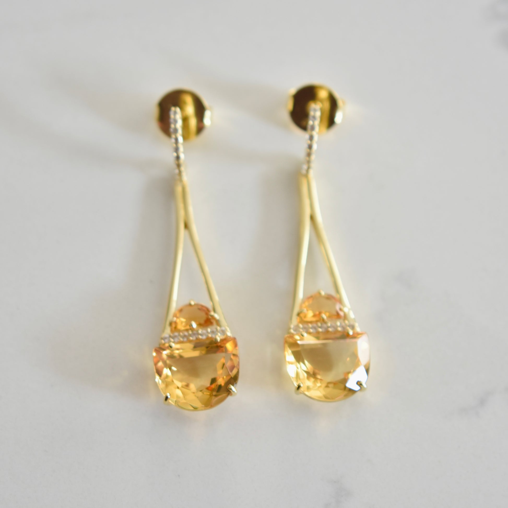 Gold earrings with teardrop-shaped citrine stones on a light gray background