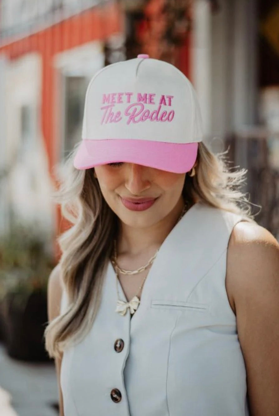 Woman wearing a cap with 'Meet Me at The Rodeo' text, standing outdoors.