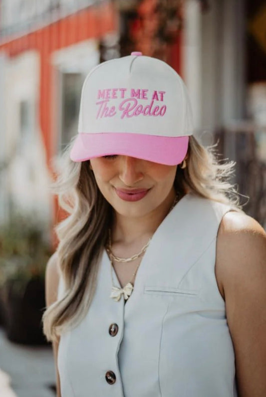 Woman wearing a cap with 'Meet Me at The Rodeo' text, standing outdoors.