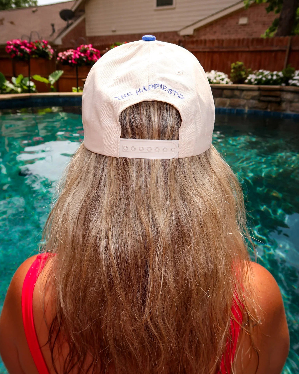Person wearing a beige cap with text, standing by a pool.