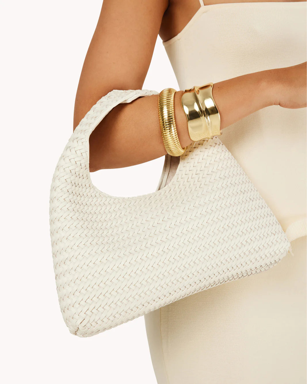 White woven handbag held by a person wearing gold bracelets on a white background