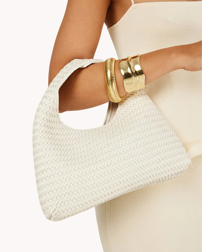 White woven handbag held by a person wearing gold bracelets on a white background
