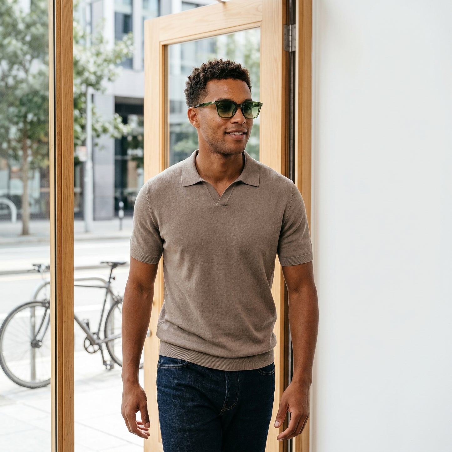 Man wearing sunglasses and a brown polo shirt standing near a door.