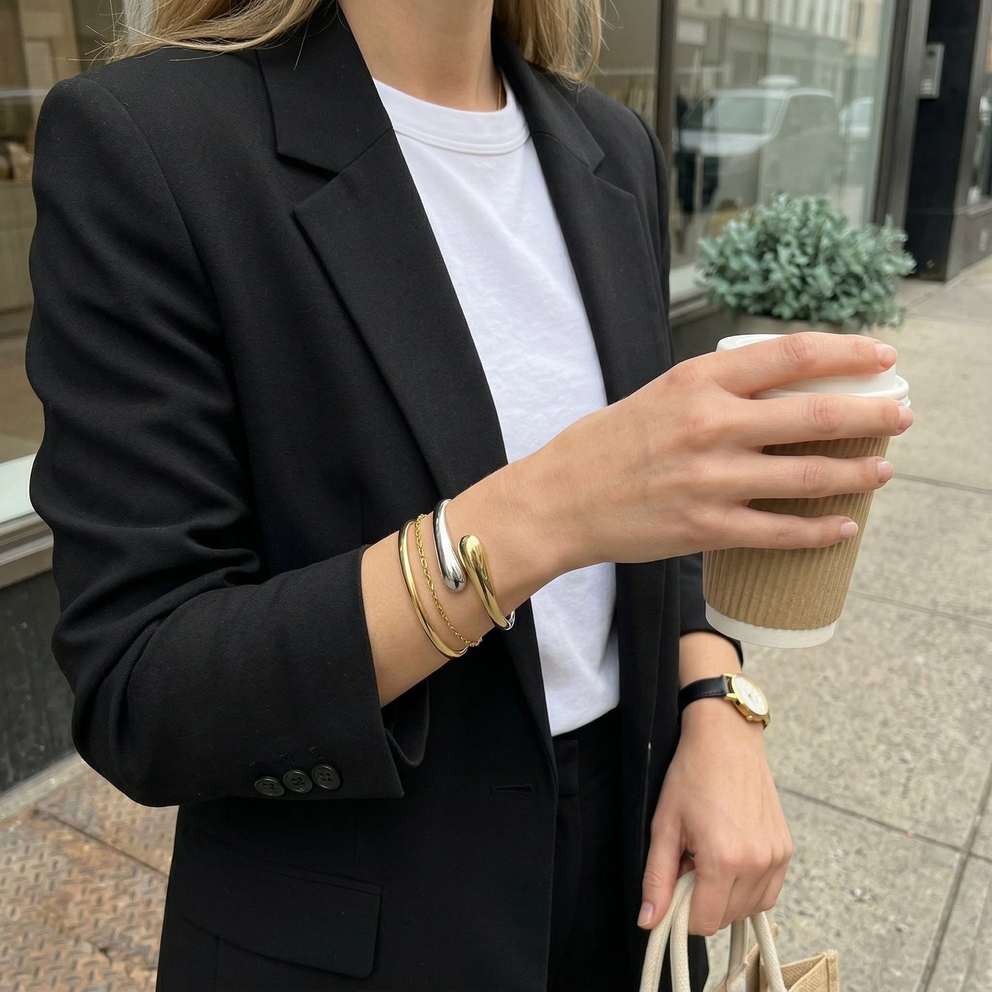Person in a black blazer holding a coffee cup outdoors.