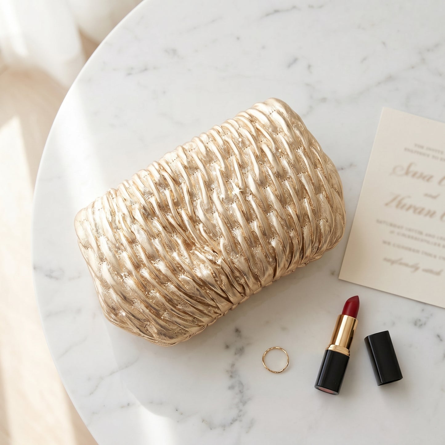 Beige woven clutch on a marble surface with lipstick and ring