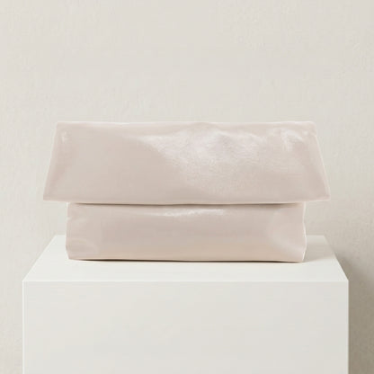 Folded light pink fabric on a white pedestal against a beige background